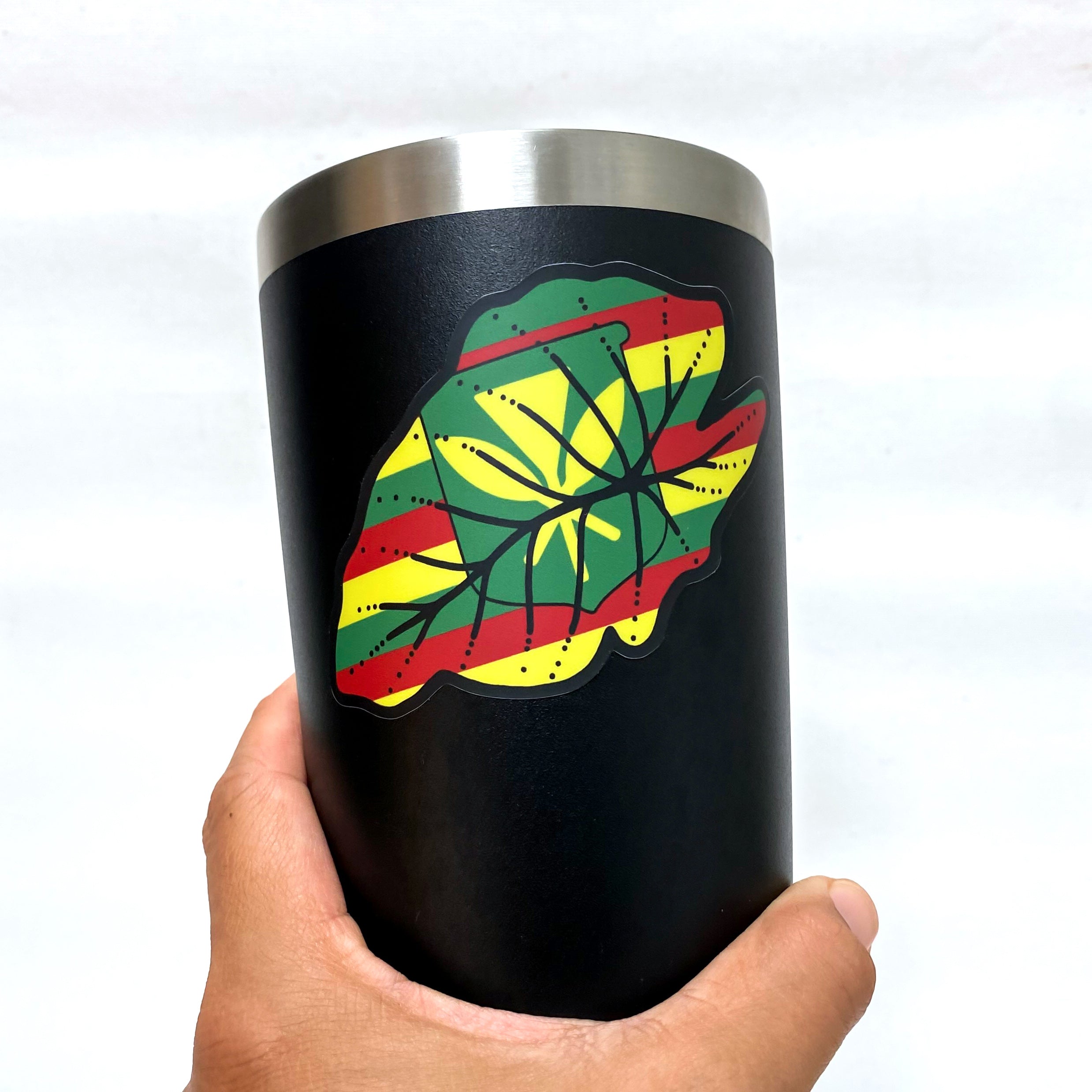 A person holds a black tumbler featuring a vibrant red, green, and yellow leaf design against a neutral background.