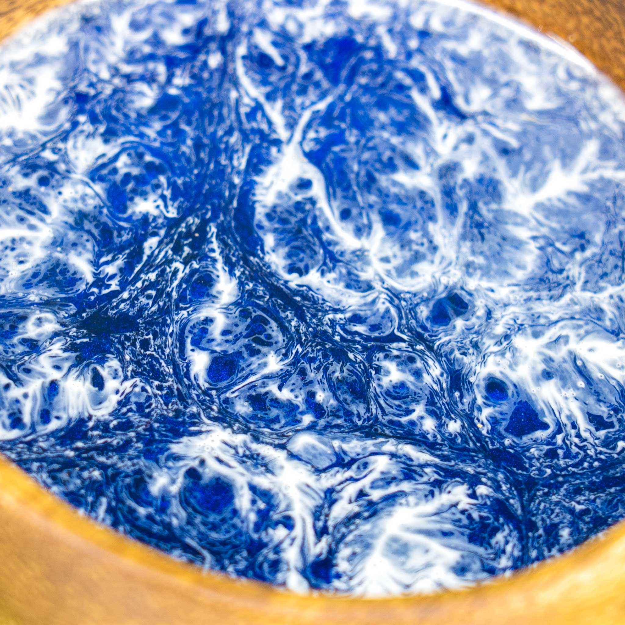 Close-up of the resin inlay in a wooden bowl, showcasing intricate marbling of deep blue and white tones that resemble foamy ocean currents.