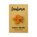 An orange and gold enamel pin shaped like a hibiscus flower, mounted on a brown card with the text 'laulima' and 'koki’o ʻula ʻula Hibiscus kokio' below it.